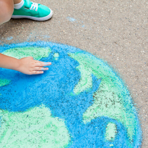 Das Bild zeigt ein Kind, dass mit Kreide die Erde auf Asphalt gemalt hat.