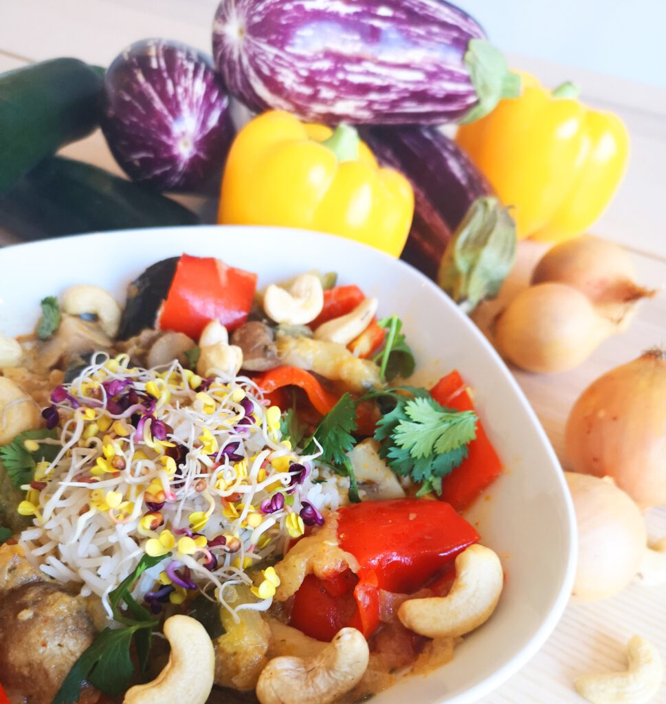 Das Bild zeigt Curry mit Cashewkernen. Im Hintergrund befindet sich Gemüse.