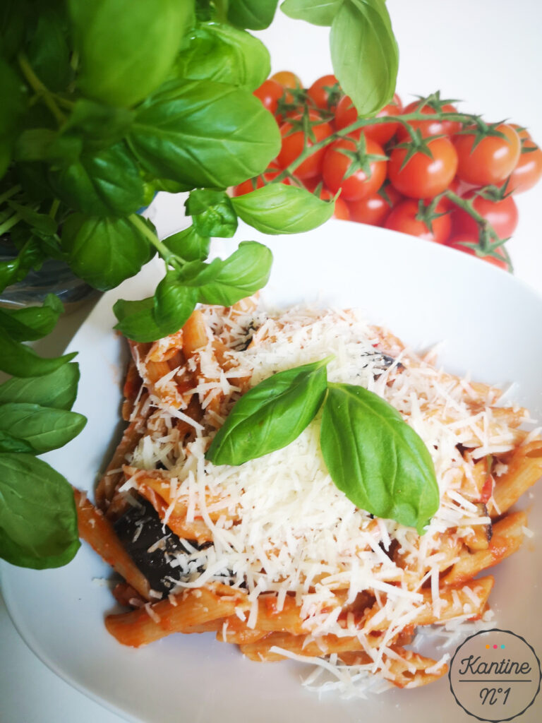 Das Bild zeigt Pasta mit Parmesan. Im Hintergrund befinden sich Tomaten und Basilikum