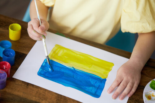 Ein Kind malt auf einem Blatt Papier eine Flagge der Ukarine