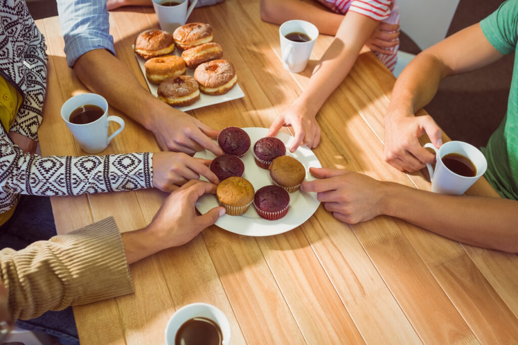 Tisch mit mehreren Personen. In der Mitte ein Teller mit Muffins und Teetassen